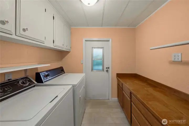 The dedicated laundry room features built-in cabinetry & a long countertop for folding, and included washer and dryer—creating an efficient and well-organized workspace.