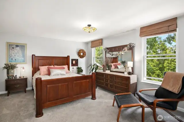 Spacious and serene primary bedroom with large windows, plush carpeting, and elegant wood furnishings.