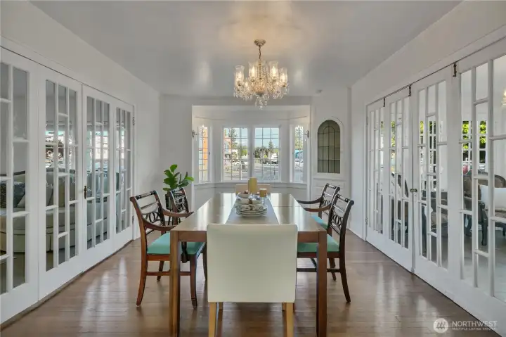 Sun-drenched dining room framed by elegant French folding doors and a classic bay window