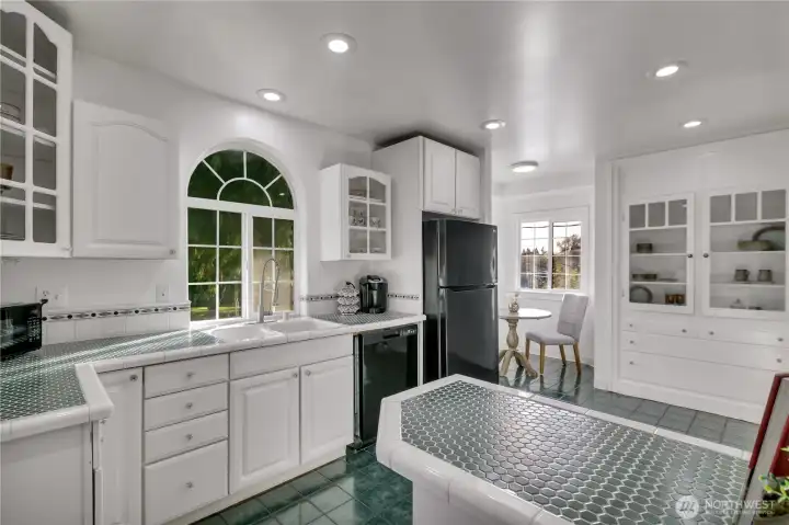 Bright kitchen featuring an arched window over the sink and classic tile countertops.