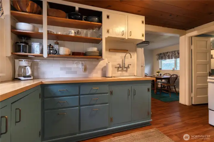 Two-toned cabinetry blends luminous white uppers w/open shelving, a modern style backsplash, and butcher block counters, delivering character and modern appeal.