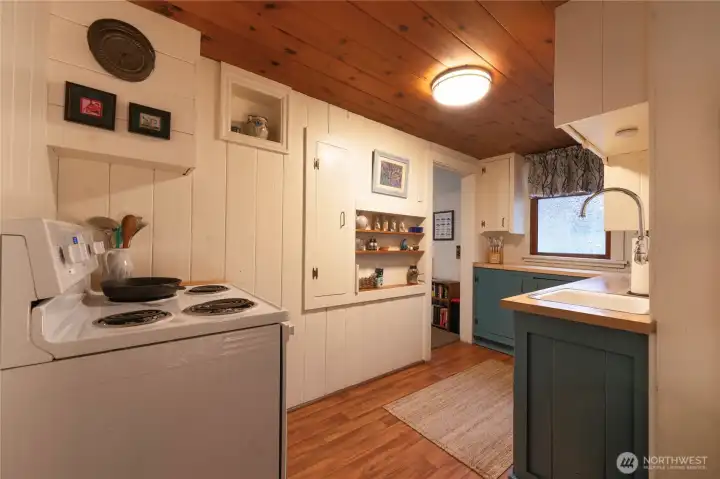 Kitchen features white panel walls, wood ceiling, vintage spice-cabinet and open shelving that adds both charm and functionality. The combination of historic character and bright, updated finishes creates an inviting workspace w/room to display curated pieces that enhance the home's timeless appeal.