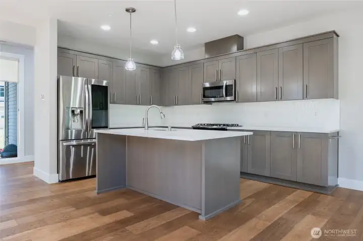 Open kitchen wtih quartz countertops, island, and gas stove