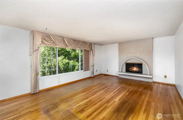 Sunlit living room boasts a large window and a distinctive arched fireplace.