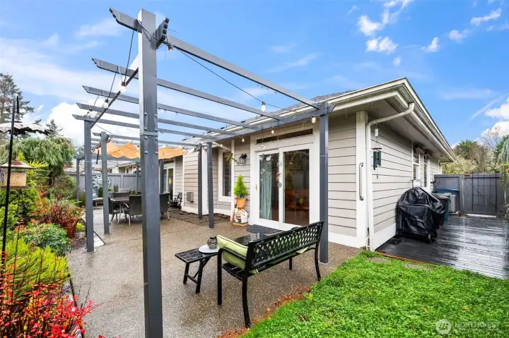 Patio with three pergolas and canvas covers and a barbecue deck at right alongside the townhome