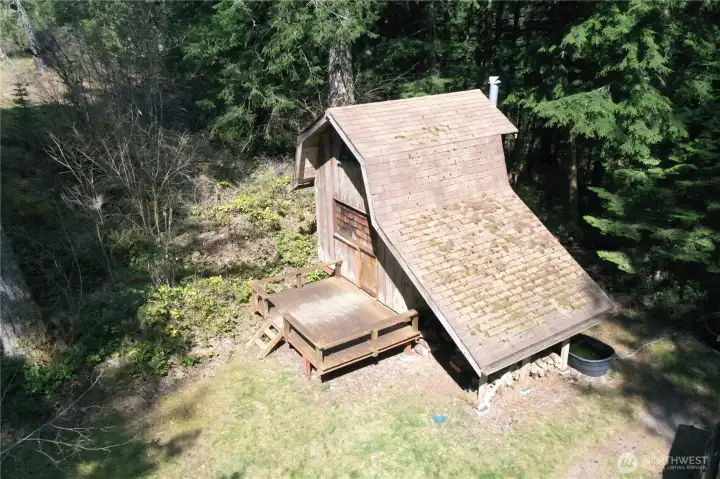 Drone shot of one room cabin with deck  If you go right upon passing through the entry gate this trail/roadway will bring you to a grove of trees and a meadow. This is adjacent to May Creek RD on the SE portion of the property