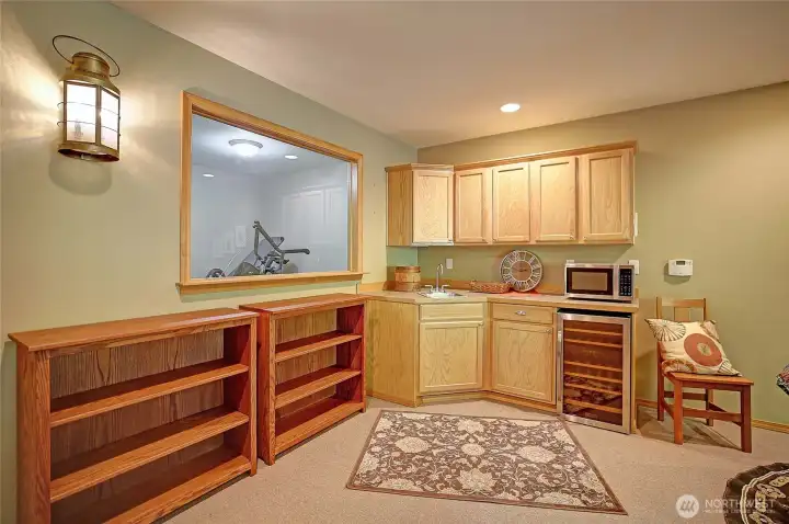 Wet bar or kitchenette with wine frig, microwave and cabinets to stash party supplies. Gym can been seen through large window on left.