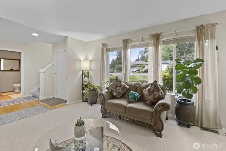 Bright living room showcasing large white vinyl windows and warm hardwoods flowing through the entry and powder room.