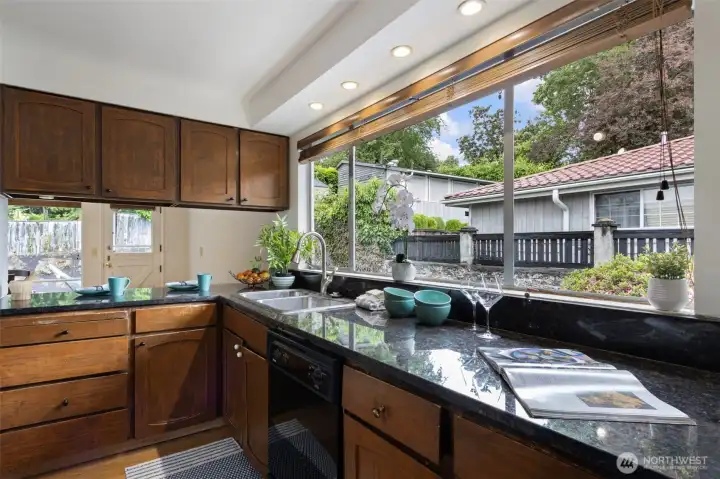 The window makes the kitchen. Granite counters, recessed lighting, yard view while you do the dishes. Pass-through to the breakfast nook and second dining area beyond.