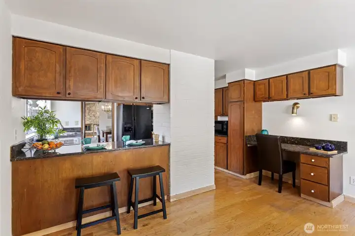 Pass-through counter with bar seating, built-in desk, painted brick column. Casual dining, homework, morning coffee — same room.