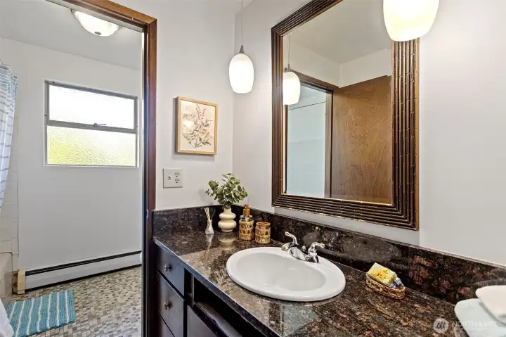 The full bath — granite counter, pendant lighting, mosaic tile floor, tub. Well appointed for its era and ready to serve the whole main floor.