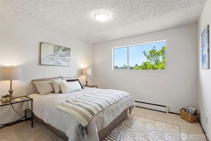 The second bedroom has room for a queen, a west-facing window full of trees, and brand-new carpet underfoot.