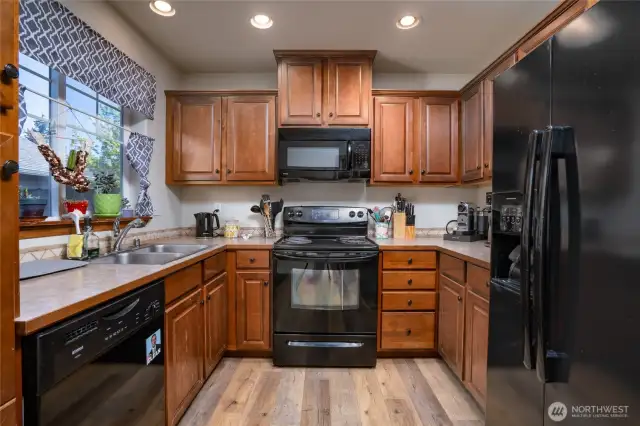 Kitchen with laminate flooring. Black appliances compliment the wood cabinets nicely.