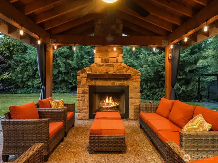 The covered back patio provides a cozy retreat with a wood-burning fireplace for chilly evenings. Dual built-in electric heaters ensure year-round comfort, while a ceiling fan with integrated lighting adds functionality and ambiance. Curtains offer privacy, making it perfect for relaxation and entertaining in any season.