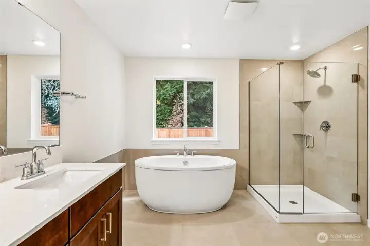 Freestanding soaking tub and glazed shower enclosure with tile surrounds and tile flooring.