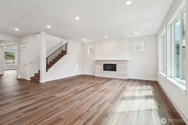 View from the Nook to great room. Gas fireplace and large mantel. Open black rail and LVP flooring on main level and at stairs & upper hall.