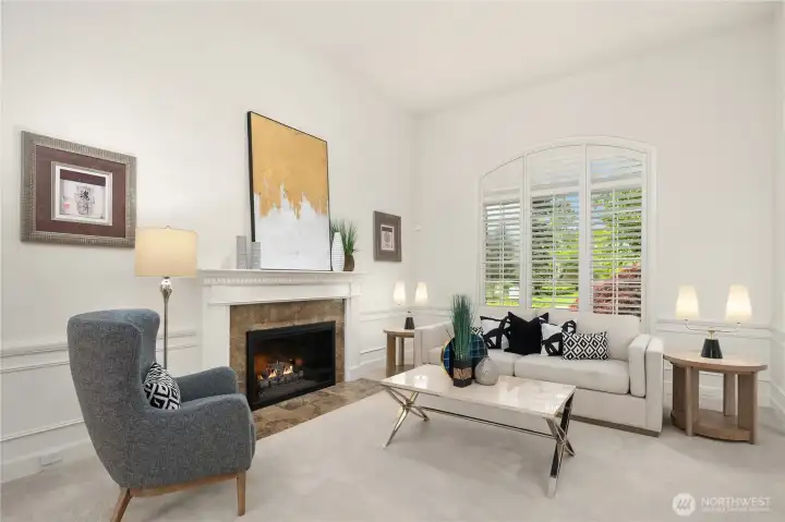 This view from the formal dining room showcases the beautiful marble tile faced fireplace in this entertainment-sized living room.  The large gracefully arched window has high quality plantation shutters for light or privacy.