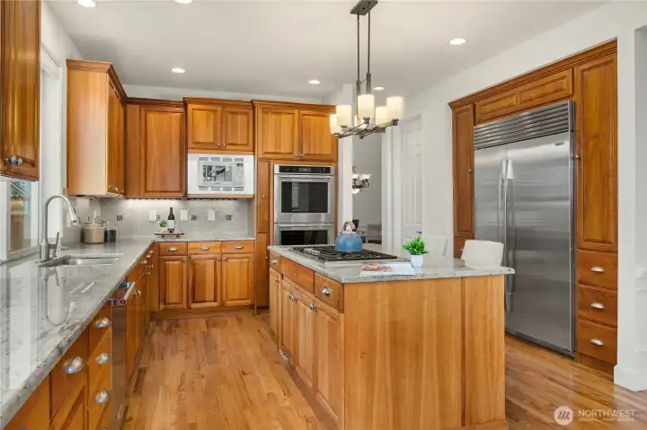 The large capacity,  built-in Sub Zero refrigerator is featured on the right, framed by storage cabinets and drawers.  With an abundance of cabinets in this kitchen, there is also a walk-in pantry to the left of the fridge.