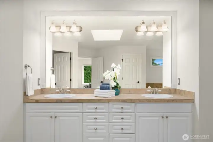 The spa-like bath adjoining the primary suite has a pristine double sink vanity. generous storage space, and a large beautifully framed mirror.  Reflected in the center of the mirror, is a skylight that floods the room with light.