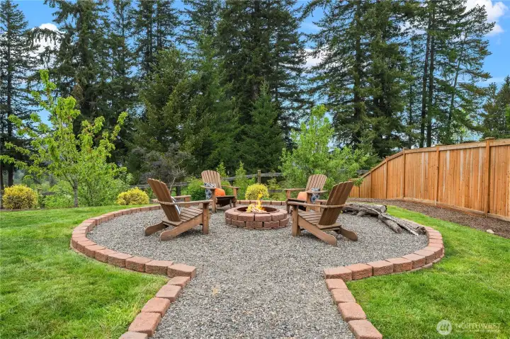 Very large custom designed fire pit flows from gazebo and is framed by spacious lawn and green space backdrop.