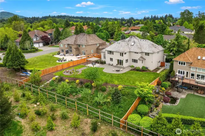 Aerial photo shows home's estate-size lot with stone path to gardens and fruit trees on property, with green space on other side of the perimeter fence.
