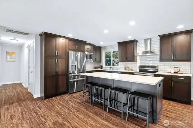??? Stunning Chef’s Kitchen – Modern, Spacious & Inviting!  This beautifully remodeled kitchen is the heart of the home, featuring rich espresso cabinetry, sleek quartz countertops, and a full-height subway tile backsplash for a timeless touch. Stainless steel appliances, including a French-door refrigerator and a vented hood, combine style with function. The oversized island with bar seating is perfect for entertaining or casual dining. Recessed lighting and wide-plank flooring complete the space, offering warmth and elegance in every detail.