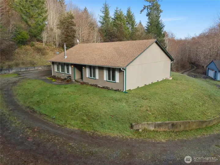 Alternate view of your rambler perched atop a clearing within your 5 acres. Fresh exterior paint and newer roof. Shop in distance to right, garage parking on left with additional RV parking. Extremely private lot with long driveway to clearing.