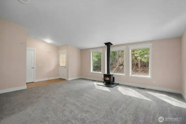 Alternate view of your expansive vaulted living space towards the front entryway. Coat closet directly off entryway, and another view of the fantastic fireplace and light filled windows. Notice the serene surroundings outside windows creating privacy and a natural barrier.