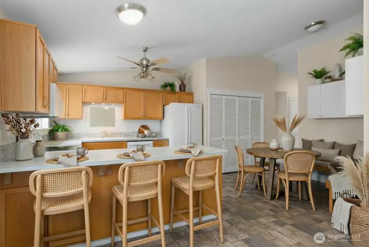 A view from the additional living space off kitchen into your beautiful open-concept space. Photo shows a virtual representation of how space could be utilized with kitchen nook seating and barstools. Kitchen is nice and bright with natural light and plenty of room to move around.