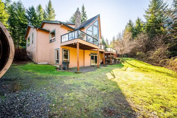 Exterior rear of home. Doors out from the basement into the lawn. Main floor deck overlooks the greenery outside.