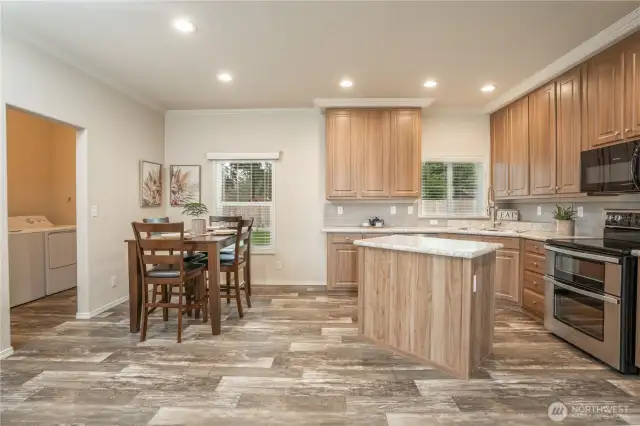View of kitchen and dining area, notice the nice details with crown molding, tile back splash, and valances on windows. Plus all appliance convey. Doorway on the left is the utility room.