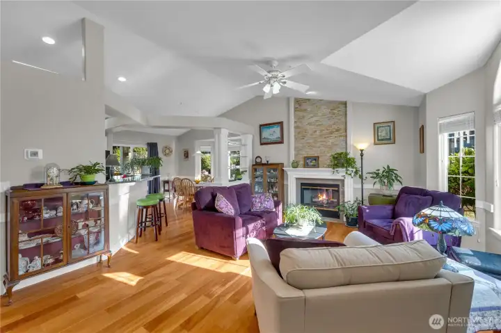 Nice and spacious with vaulted ceilings and hardwood floors, this open-concept living area features a cozy gas fireplace framed by stone accents. Natural light fills the room, flowing seamlessly into the dining area and kitchen—perfect for relaxing or entertaining.
