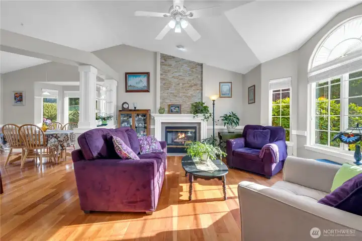 Elegant and airy, this living room promotes vaulted ceilings, rich hardwood floors, and a stunning stone-accented gas fireplace. Sunlight pours through large windows, creating a warm and welcoming space for relaxing or entertaining.