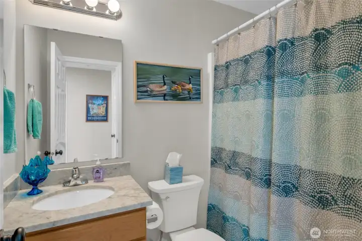 Charming and bright bathroom featuring a marble-style vanity, soft neutral tones, and a full shower/tub combination—designed for comfort and functionality.
