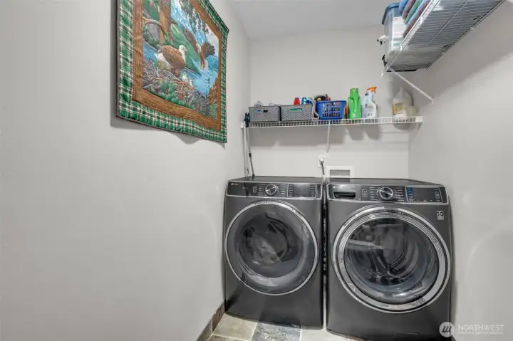 Efficient laundry space with modern front-load washer and dryer, tile flooring, and convenient shelving for storage and organization.