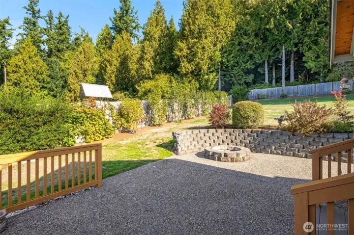 Beautifully landscaped backyard with a spacious patio and built-in fire pit, perfect for outdoor gatherings. Surrounded by mature trees and garden beds, this peaceful space offers privacy and plenty of room to relax or play.