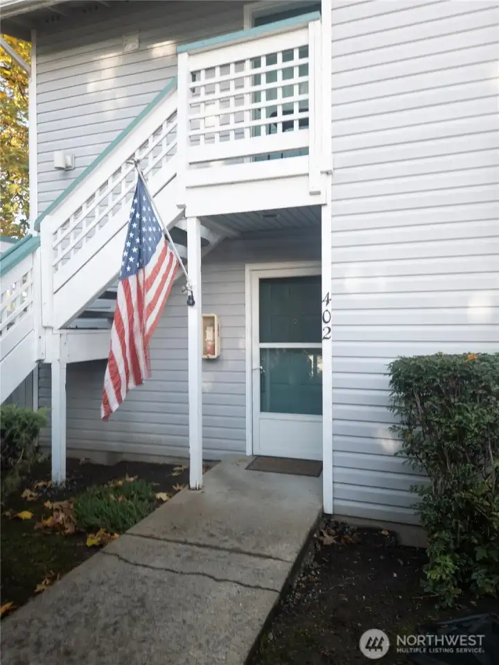 Welcoming walkway to unit 402, featuring a ground-level entrance with a covered porch and easy access from the parking area.