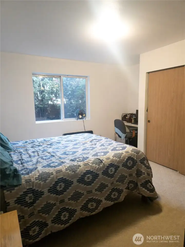 The primary bedroom offers a peaceful retreat with a large window that looks out to mature greenery, creating a quiet and private atmosphere. The room provides comfortable space for a full bedroom setup, along with a convenient closet and room for a small desk or reading nook.