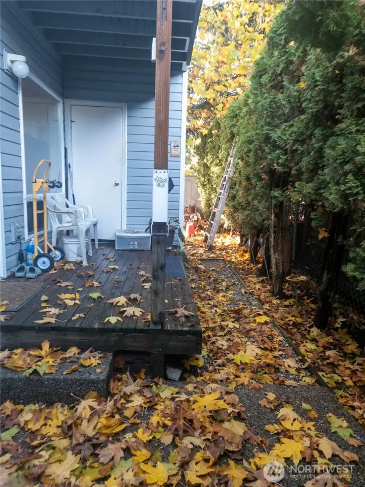 This view highlights the covered back entry and small deck area, offering a sheltered spot for seating or storage. Mature hedges along the fence line add privacy, making this outdoor space feel tucked away and comfortable.