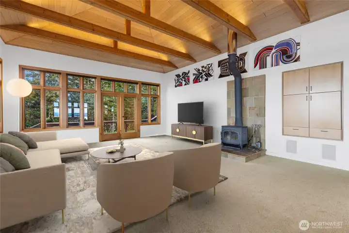 Light-filled living room with soaring ceilings, exposed beams, and a cozy wood stove, designed to capture water views and create a warm, inviting gathering space.