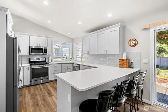 Newly updated kitchen with soft closing white cabinetry, subway pattern deco tile backsplash, quartz countertops, stainless steel appliances, and walk in pantry space in laundry room.