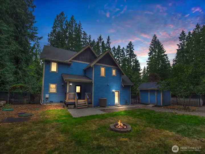 Twilight shot of the back yard. Back elevated porch leads to the main kitchen. Lit door on the right leads to the secondary small kitchen.