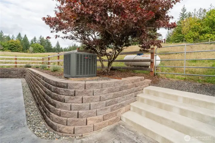 Sidewalk between front and back, with AC unit & propane tank. Stairs lead to the back of the garage for the upper loft entrance. (Other entrance for loft located inside garage with a pull-down staircase)