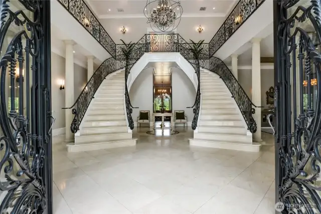 Grand imported glass-and-iron doors that open into a breathtaking entryway. Inside, dual curved, Italian marble staircases with custom iron scrollwork rise beneath curated Restoration Hardware lighting.