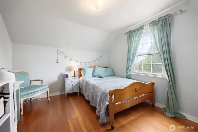 Upper level bedroom with a bright light window and natural wood flooring. This warm space is a wonderful, restful sanctuary.