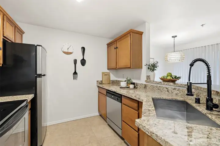 Updated kitchen featuring granite countertops, stainless steel appliances, warm wood cabinetry, and a stylish matte black pull-down faucet with pendant lighting over the pass-through.