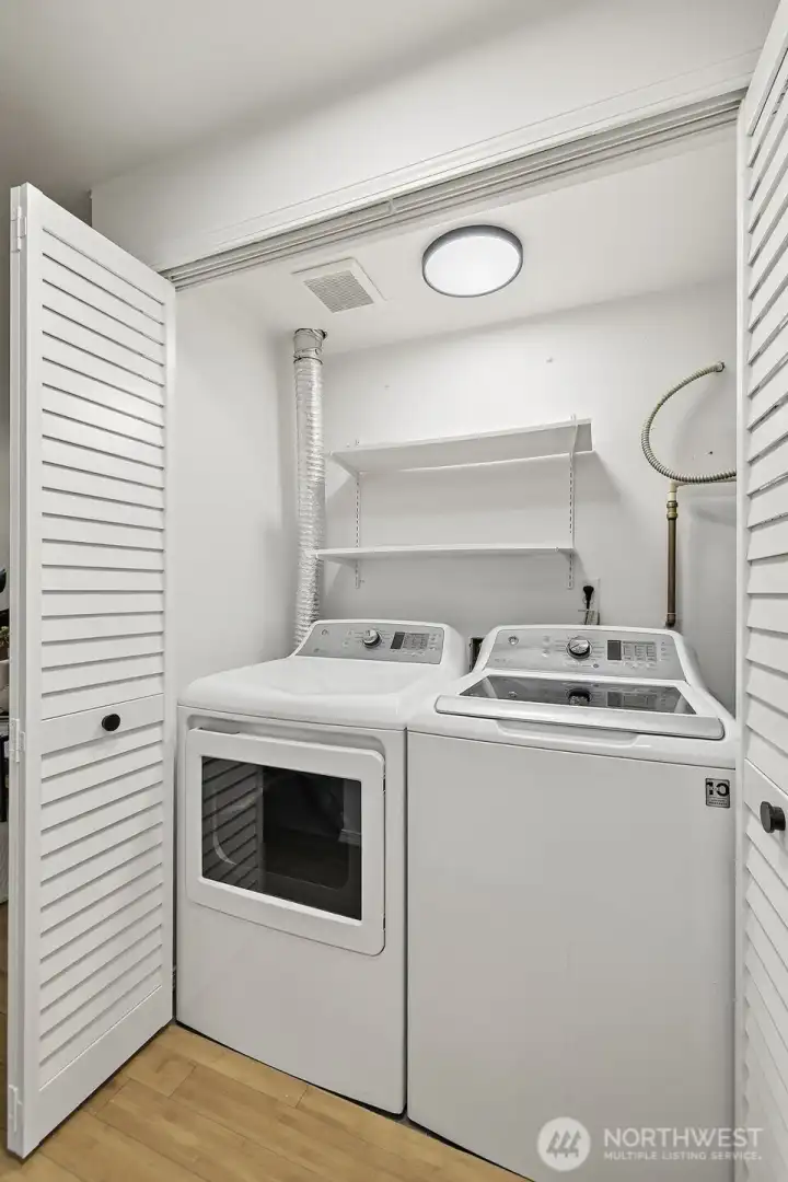 Full-size washer and dryer tucked neatly behind louvered doors with overhead shelving for added storage.
