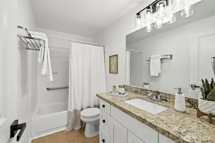 Updated full bath with granite vanity, white cabinetry, modern globe light fixture, and tub/shower combo.