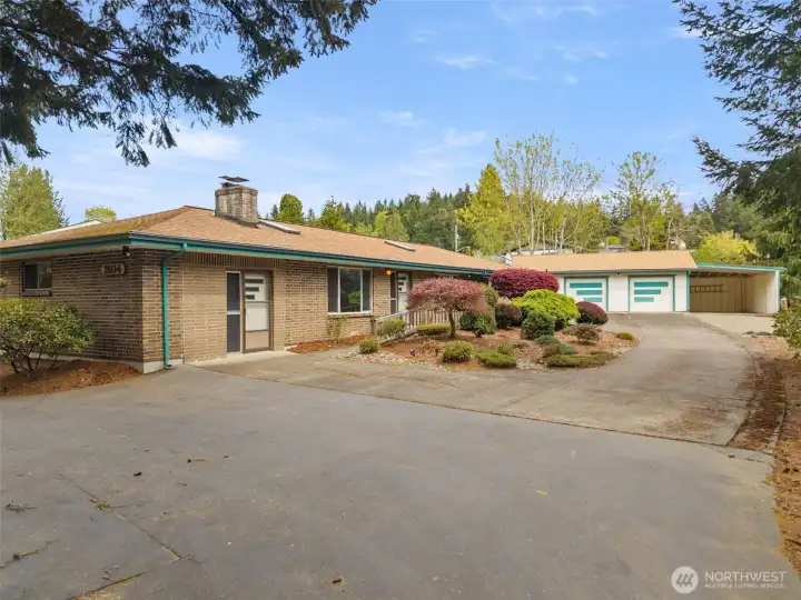 The expansive paved driveway, huge detached garage, and mature landscaping create such a welcoming first impression here. There’s a subtle mid-century feel to the approach, and the classic brick exterior gives the home a timeless sense of character.