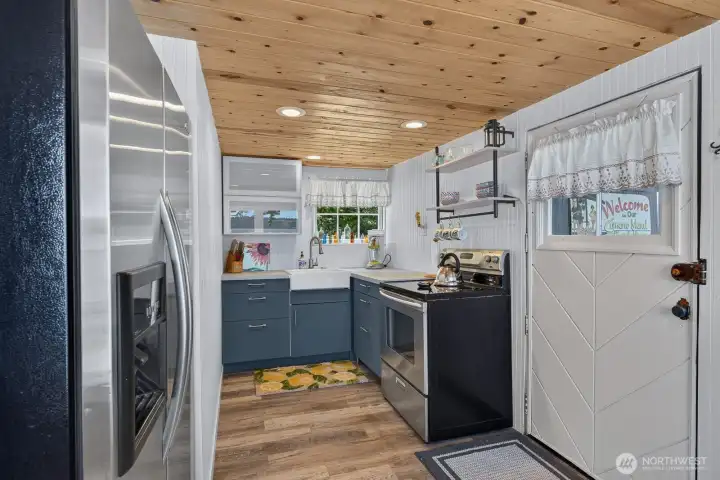 Bright, updated kitchen featuring stainless steel appliances, open shelving, warm wood ceilings, and a functional layout designed for easy everyday living.